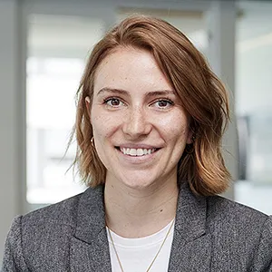 Portrait einer jungen Frau mit rotbraunen Haaren und grauem Blazer. Sie blickt lächelnd in die Kamera