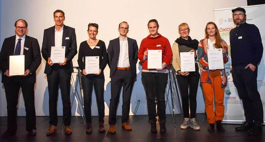 4 Männer und 4 Frauen stehen auf einem Podium. 6 davon halten lächelnd ein Zertifikat vor sich.